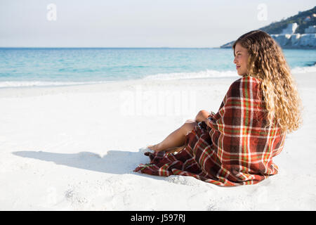 Thoughtful woman looking away while sitting on shore at beach Stock Photo