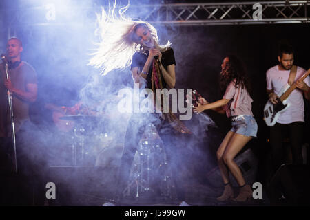 Cheerful female singer with musicians performing on stage during music festival at nightclub Stock Photo