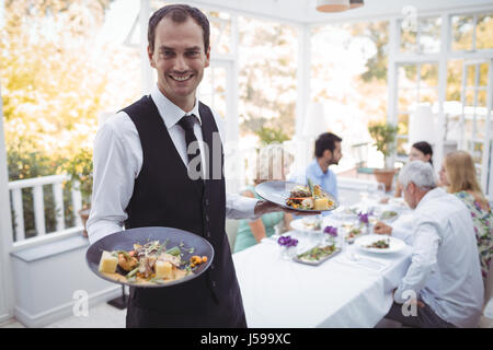 Portrait of smiling waiter holding food tray in restaurant Stock Photo