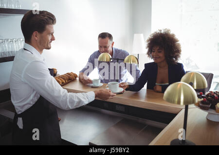 Waiter serving coffee to costumer at counter in restaurant Stock Photo