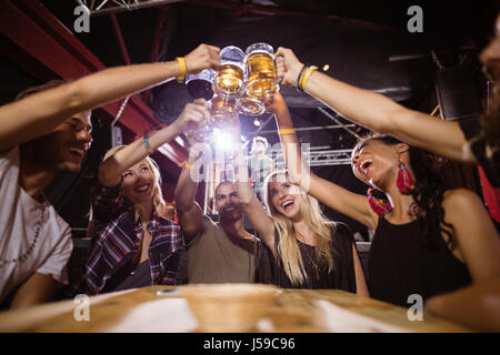 Low angle view of happy friends toasting beer glasses while sitting at table in club Stock Photo