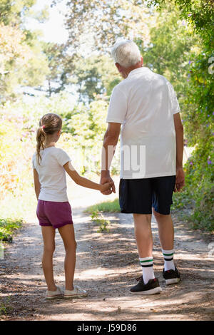 Grandfather and granddaughter holding hands while walking together in the forest Stock Photo