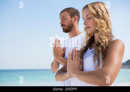 Couple with eyes closed exercising while standing at beach against clear sky Stock Photo