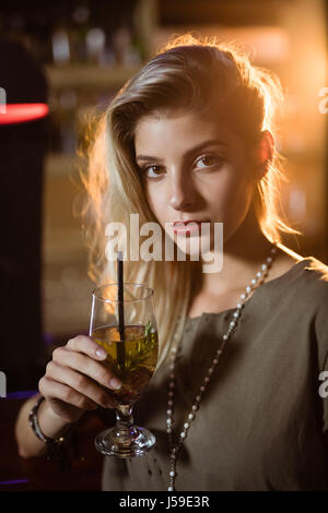 Portrait of young woman holding drink while leaning on counter in nightclub Stock Photo