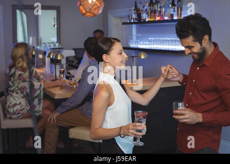 Smiling couple holding glass of drink while dancing in bar restaurant