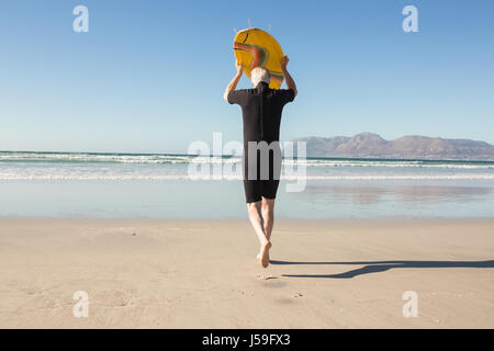 Rear view of senior man carrying surfboard at beach on sunny day Stock Photo