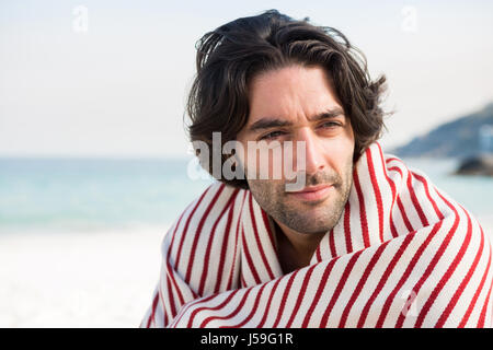 Close up of thoughtful man wrapped in shawl while sitting at beach on sunny day Stock Photo