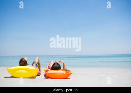 Couple relaxing on pool raft at beach against clear sky Stock Photo