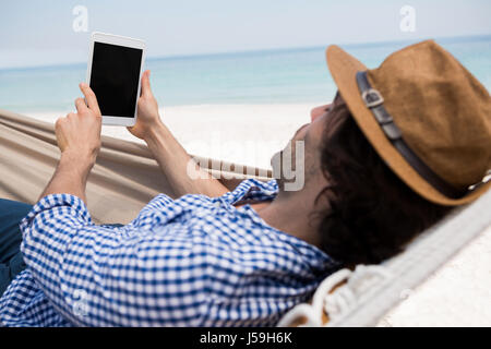 Man using tablet computer while lying in hammock at beach Stock Photo