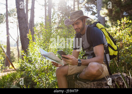 Man using mobile phone while holding the map in the forest Stock Photo