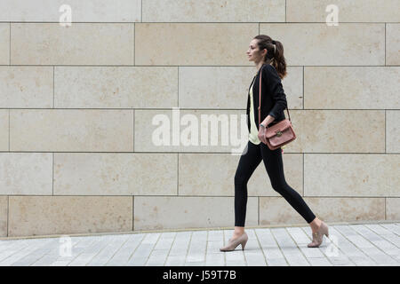 Side view of a Caucasian Businesswoman walking on city street in front of modern marble wall. Stock Photo
