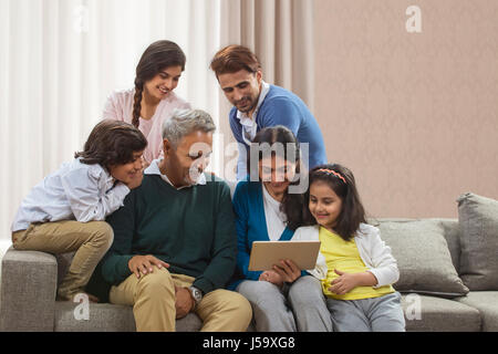 Portrait happy multi generation family using digital tablet sitting on sofa Stock Photo