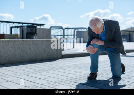 Worried senior man having problems with knee outdoors Stock Photo