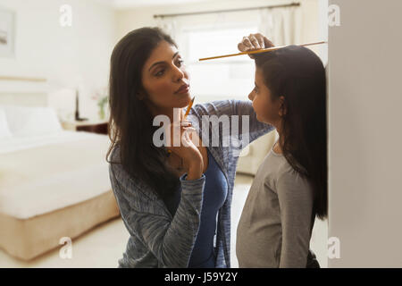 Mother keeping record of her daughter's height at home on the wall Stock Photo