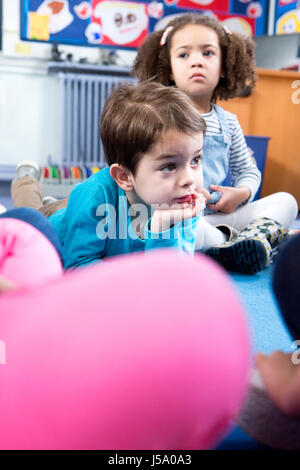 Little boy lying on the floor at nursery during story time. Stock Photo