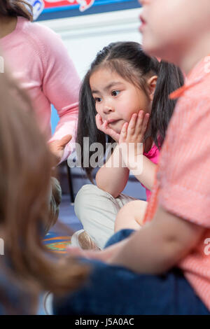 Little girl sitting with her legs crossed and her head in her hands during storytime at nursery. Stock Photo