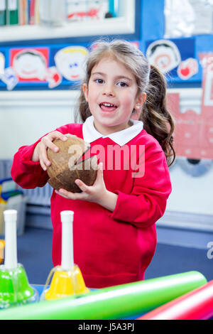 Little girl in nursery making music with coconut shells in her lesson. She is looking at the camera. Stock Photo