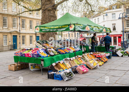 Fruit and vegetables stand or stall with a wide selection of products on display in a local town market with customer buying. Bath, UK. Stock Photo