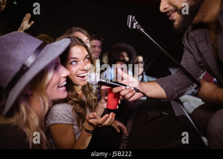 Female friends singing with male singer at nightclub during music festival Stock Photo