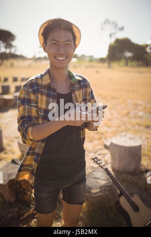 Portrait of smiling man using mobile phone while standing on field Stock Photo