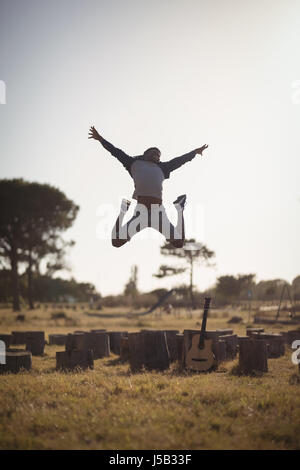 Man jumping on field against clear sky at forest Stock Photo