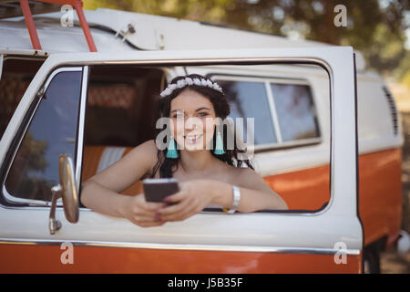 Portrait of woman using mobile phone while leaning on door of motor home Stock Photo