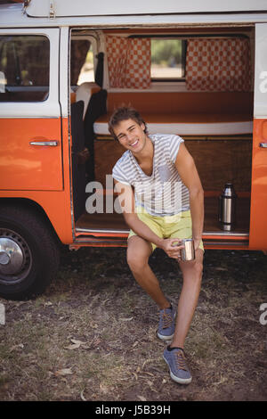 Portrait of young man drinking coffee while sitting in van at forest Stock Photo
