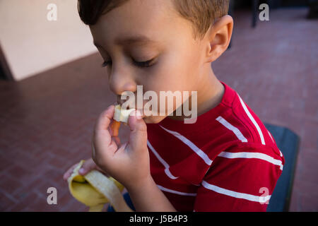 Close up of boy eating banana while sitting on chair at school Stock Photo