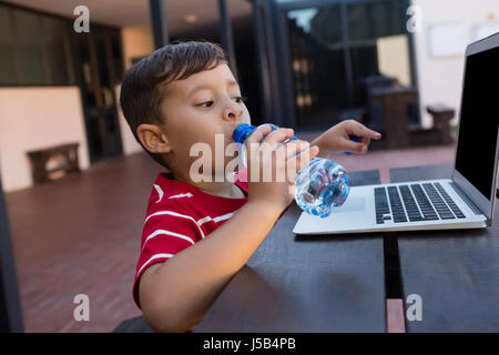 Boy drinking water while using laptop at table in school Stock Photo