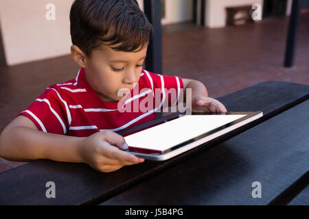 Close up of boy using digital tablet while sitting at table in school Stock Photo
