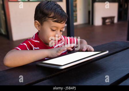 Close up of smiling boy using digital tablet while sitting at table in school Stock Photo