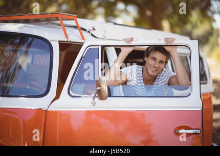Portrait of cheerful young man leaning on van at forest Stock Photo