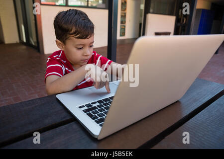 Cute boy working on digital laptop while sitting at table in school Stock Photo