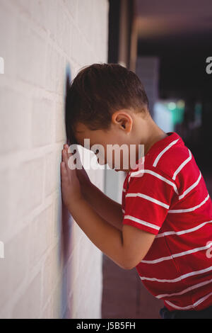 Side view of sad boy leaning on wall at school building