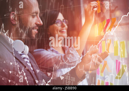 Stocks and shares against coworkers sticking adhesive notes on glass Stock Photo