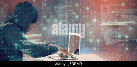 Male hacker using laptop on table  against abstract black room Stock Photo