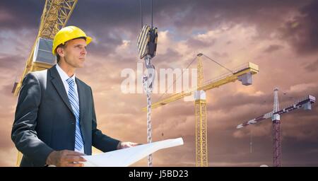 Digital composite of Architect holding blueprint against cranes Stock Photo