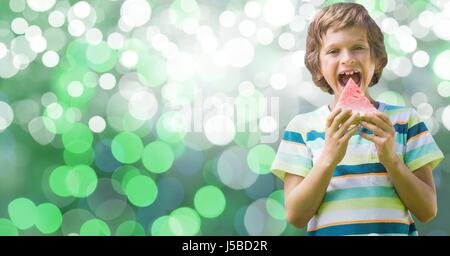 Digital composite of Boy eating watermelon over bokeh Stock Photo