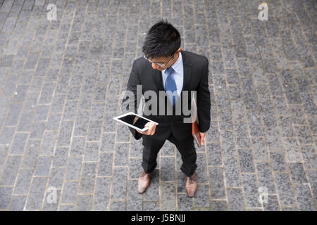 High angle view of a Chinese man standing on city street using a tablet device. Stock Photo