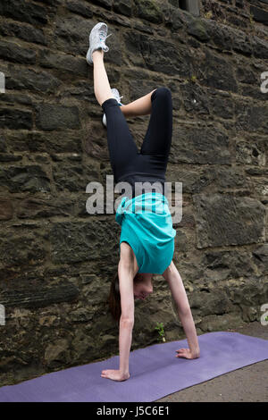Athletic woman doing a handstand against a wall. Action and healthy lifestyle concept. Stock Photo