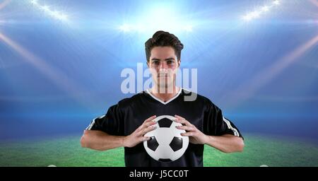 Digital composite of Confident player holding soccer ball at stadium Stock Photo