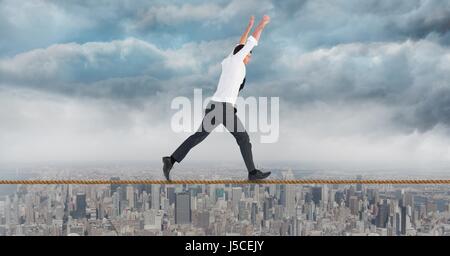 Digital composite of Businessman with arms raised walking on rope against cityscape Stock Photo