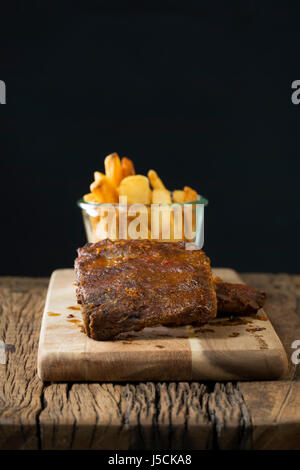 BBQ pork ribs and french fries sitting on a rustic wooden table. Stock Photo