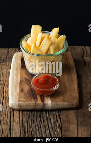 Fresh french fries or hot potato chips served in a glass bowl. The food is sitting on a rustic wooden background. Stock Photo