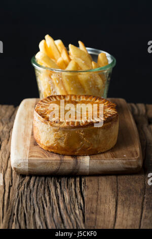 A Traditional British meat pie and chips sitting on a rustic wooden table. Stock Photo