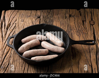 Raw gourmet butchers sausages in a frying pan, on a rustic wooden background. Stock Photo