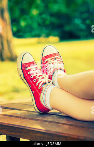 Woman's feet in a red canvas sneakers with colorful socks, sitting on a bench Stock Photo