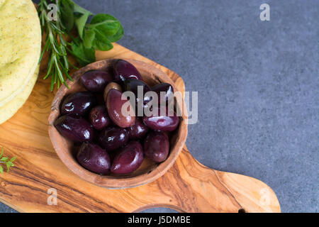 Mediterranean appetizer antipasti tapas calamara olives and garlic pita bread, herbs on wooden plank made from olive tree and grey background Stock Photo