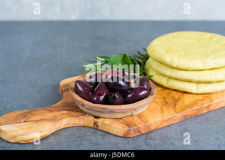 Mediterranean appetizer antipasti tapas calamara olives and garlic pita bread, herbs on wooden plank made from olive tree and grey background Stock Photo