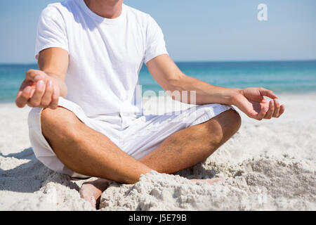 Low section of man doing meditation while sitting at beach Stock Photo
